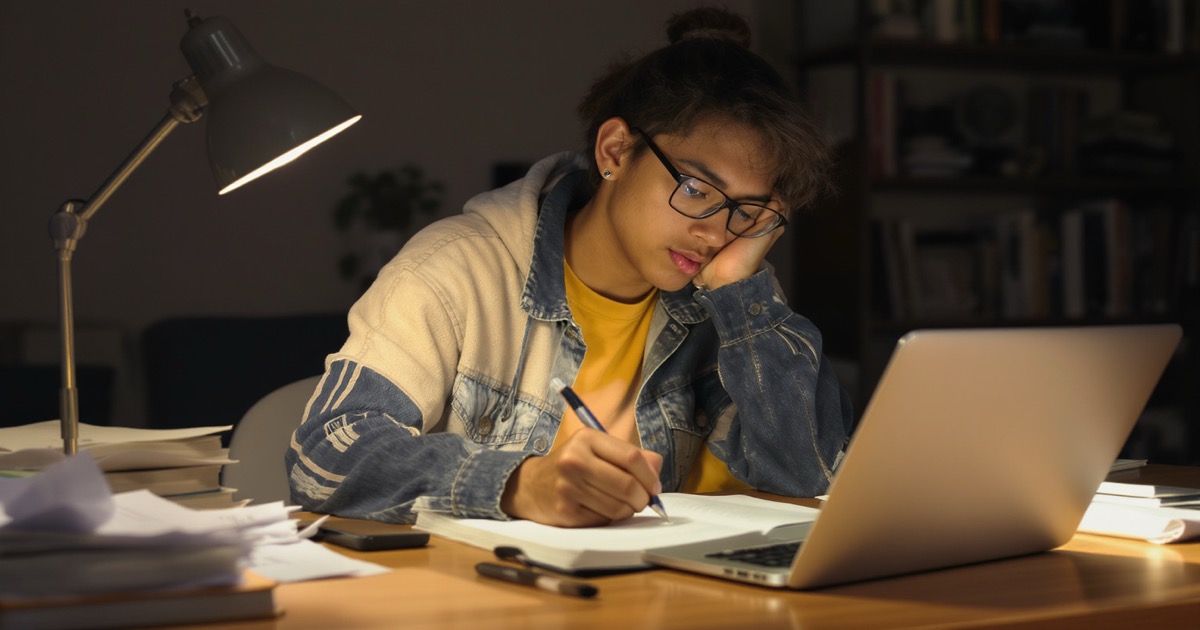 Student writing a scholarship essay at a desk with notes and laptop